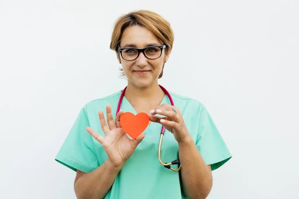 A smiling nurse in scrubs and a stethoscope holding a paper heart