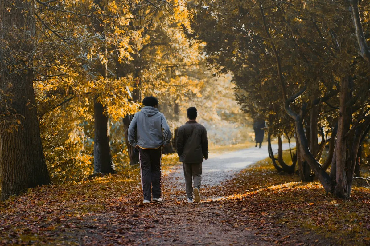 A couple walking together down a woodland path covered in autumn leaves