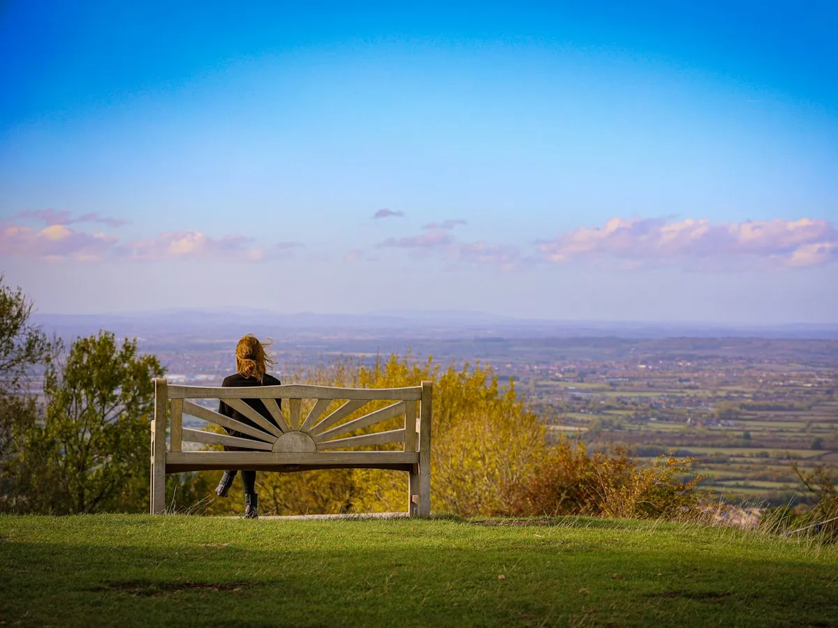 A woman sitting on a bench looking out over a wide green valley