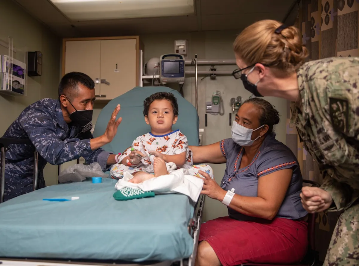 A young child sitting calmly on a medical bed while caring adults attend to them in a bright clinical room