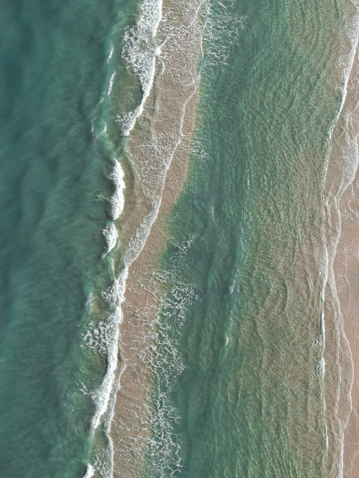 Aerial view of turquoise waves rolling onto a sandy coastline