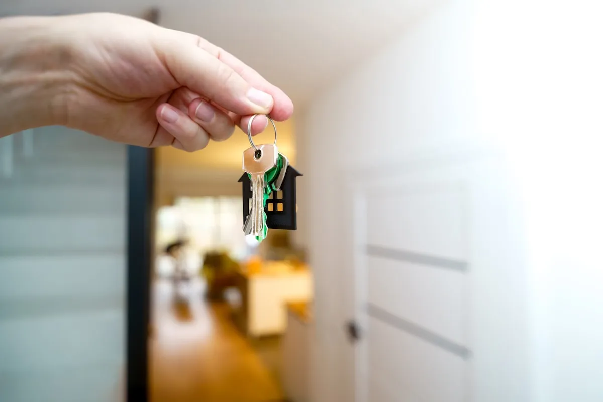 A hand holding keys in front of the entrance to a new home