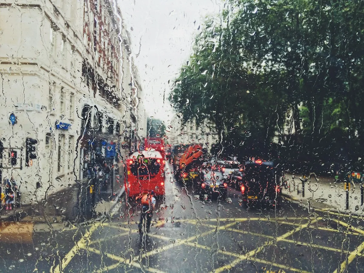 A rainy London street seen through a wet window, with red double-decker buses in the traffic